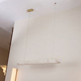 Zenvia LED Alabaster Linear Chandelier in Soft White, a horizontal alabaster cylinder pendant on twin brass cables from a slim ceiling fixing, shown against a plain wall.