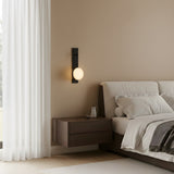Minimalist bedroom featuring a floating wooden nightstand, the Marvello LED Sculpted Disc Alabaster Wall Light in Soft White & Matte Black above, a bed with white bedding, sheer curtains over the window, and a serene neutral color palette.