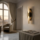 A softly lit, elegant room features a curved armchair by a tall window with cream curtains, marble floor, and the Virexa LED Oval Backplate Alabaster Wall Light in Soft White & Black. An open book rests on a fabric-covered bench under natural light.
