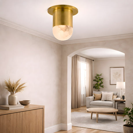 A bright living space features beige walls, a wooden sideboard with decor, and the Orvani LED Mini Drop Alabaster Semi-Flush Ceiling Light in Soft White & Brushed Brass. An archway leads to a cozy sitting area with sofa, round coffee table, lamp, plants, and wall art.