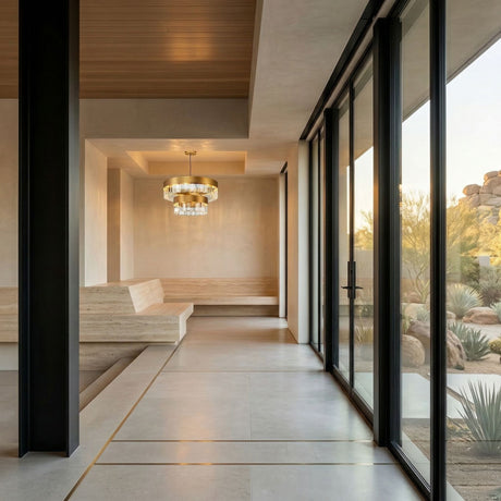 A modern, minimalist interior with floor-to-ceiling windows, a wooden ceiling, neutral walls, a beige built-in bench, and the Donato 12 Light Crystal Chandelier - Gold. Desert landscaping is visible outside.