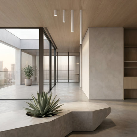 A modern, minimalist interior with concrete floors, light wood ceiling featuring the Pulcra Tube Flush Ceiling Light - White, built-in shelves, two potted agave plants, floor-to-ceiling windows, and a city building view.