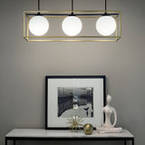 A modern interior showcases the Dawn 3 Suspension Light in brass and black with three spherical bulbs above a table. The table exhibits a framed black and white photo, a sleek abstract sculpture, and a starburst ornament, all accentuated by the chic contrast of brass and black tones.