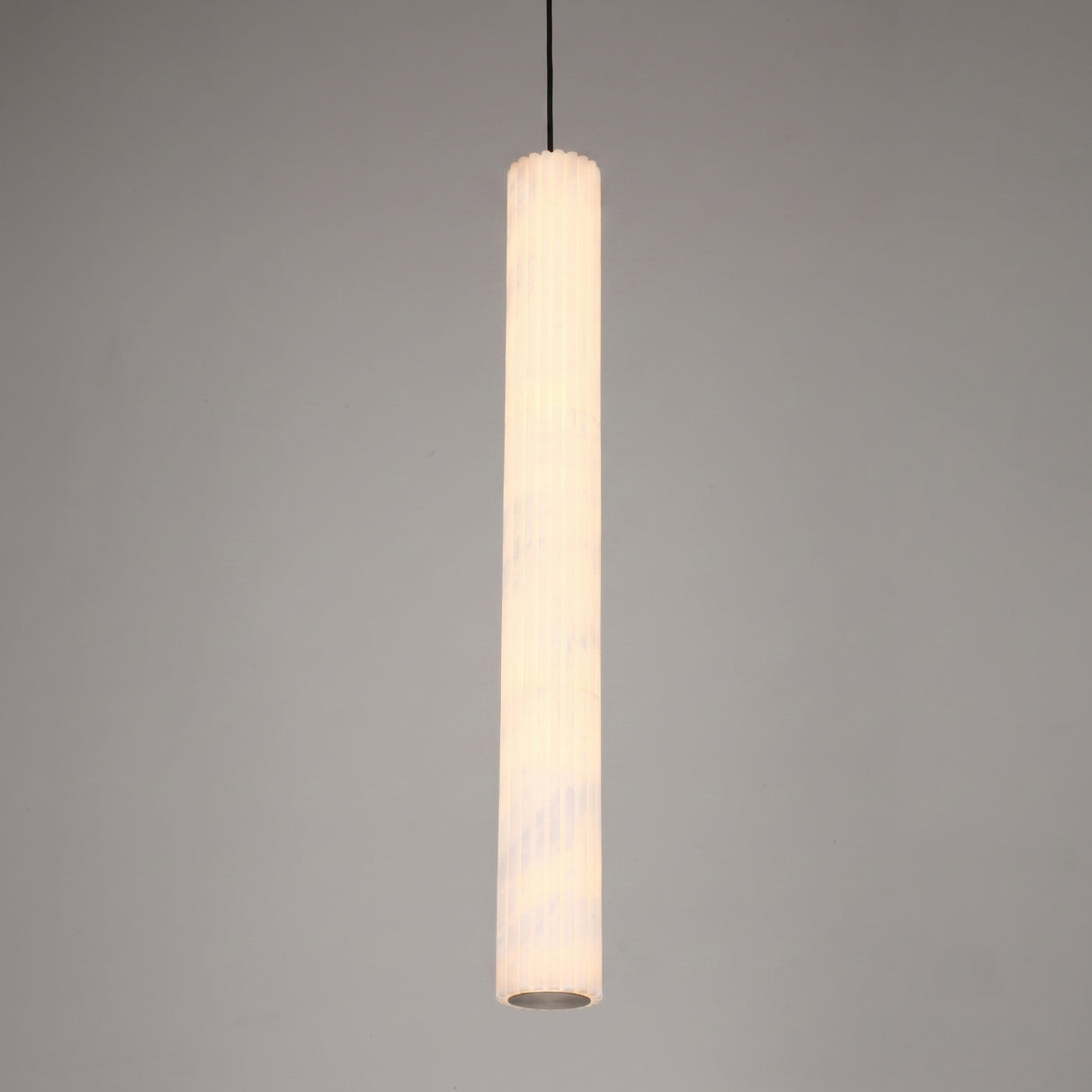 Zenvia LED alabaster single pendant light, slim fluted column with brushed brass cap and black drop cable, warm white glow, plain grey background.