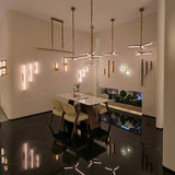 Elvaris LED Small Vertical Alabaster Wall Light in brushed brass, shown illuminated among multiple wall lights in a modern dining room with marble flooring.