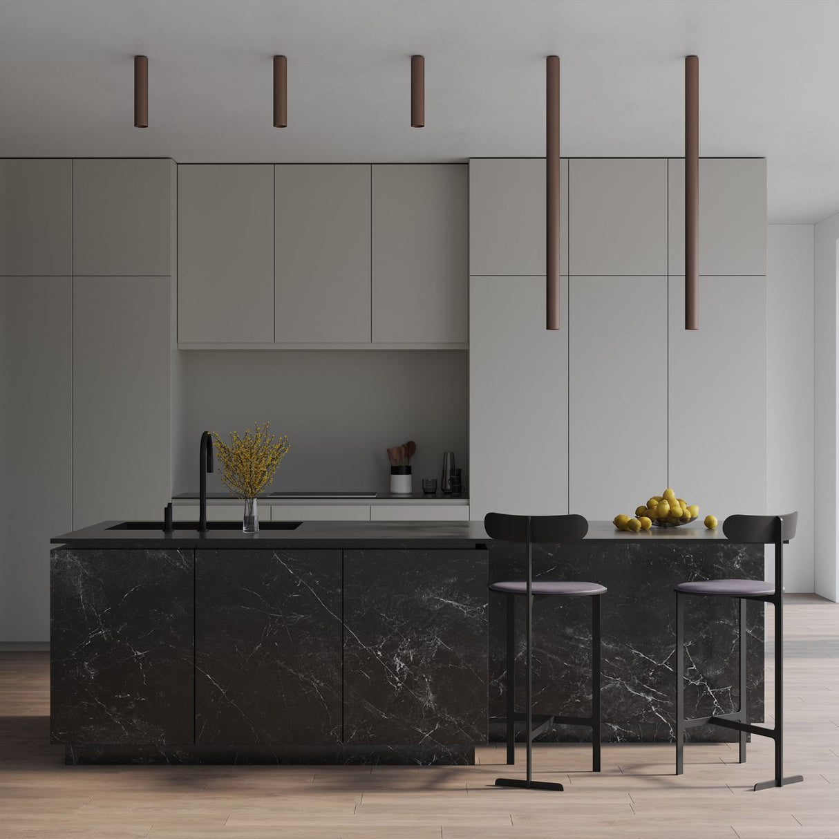 A modern kitchen showcases a black marble island with two black bar stools. The minimalist cabinets are light gray, complemented by a countertop featuring a black sink and a bouquet of yellow flowers. Pulcra LED Tube Ceiling Lights in copper hang above, enhancing energy efficiency, while a bowl of lemons rests on the counter.