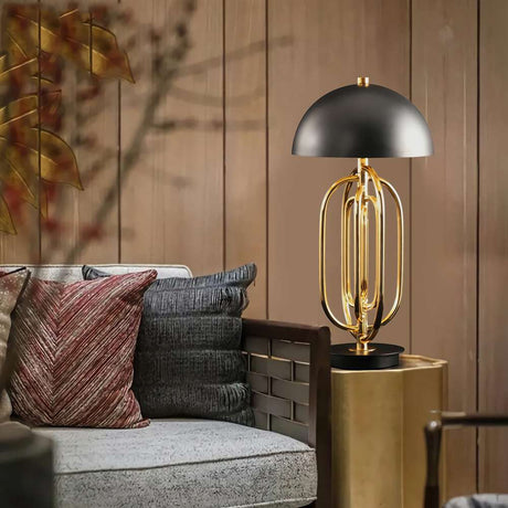A modern living room showcases the Ascot 4 Light Small Table Lamp in black and gold on a side table, providing adjustable lighting. The space includes a cozy sofa accompanied by textured cushions, while a wooden panel wall in the background is embellished with autumn-themed decor.
