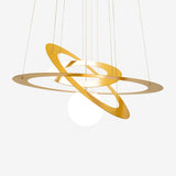 The Universe Dimmable LED Suspension Light in matte gold features a modern design with three oval rings surrounding a central white globe light. These dimmable LED rings are suspended from the ceiling and positioned at varying angles, offering an abstract, orbit-like appearance against a simple backdrop.