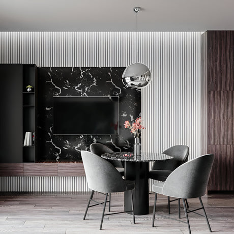 A modern dining area featuring a round black marble table, four gray upholstered chairs, a black marble wall with TV, vertical white paneling, and a Lava Small LED Pendant Light - Silver with adjustable cable lighting above the table and pink flowers in a vase.