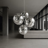 The Lava 4 Light LED Chandelier in silver hangs in a modern, minimalist lobby featuring large windows, grey tiled floors, and sleek neutral furnishings.