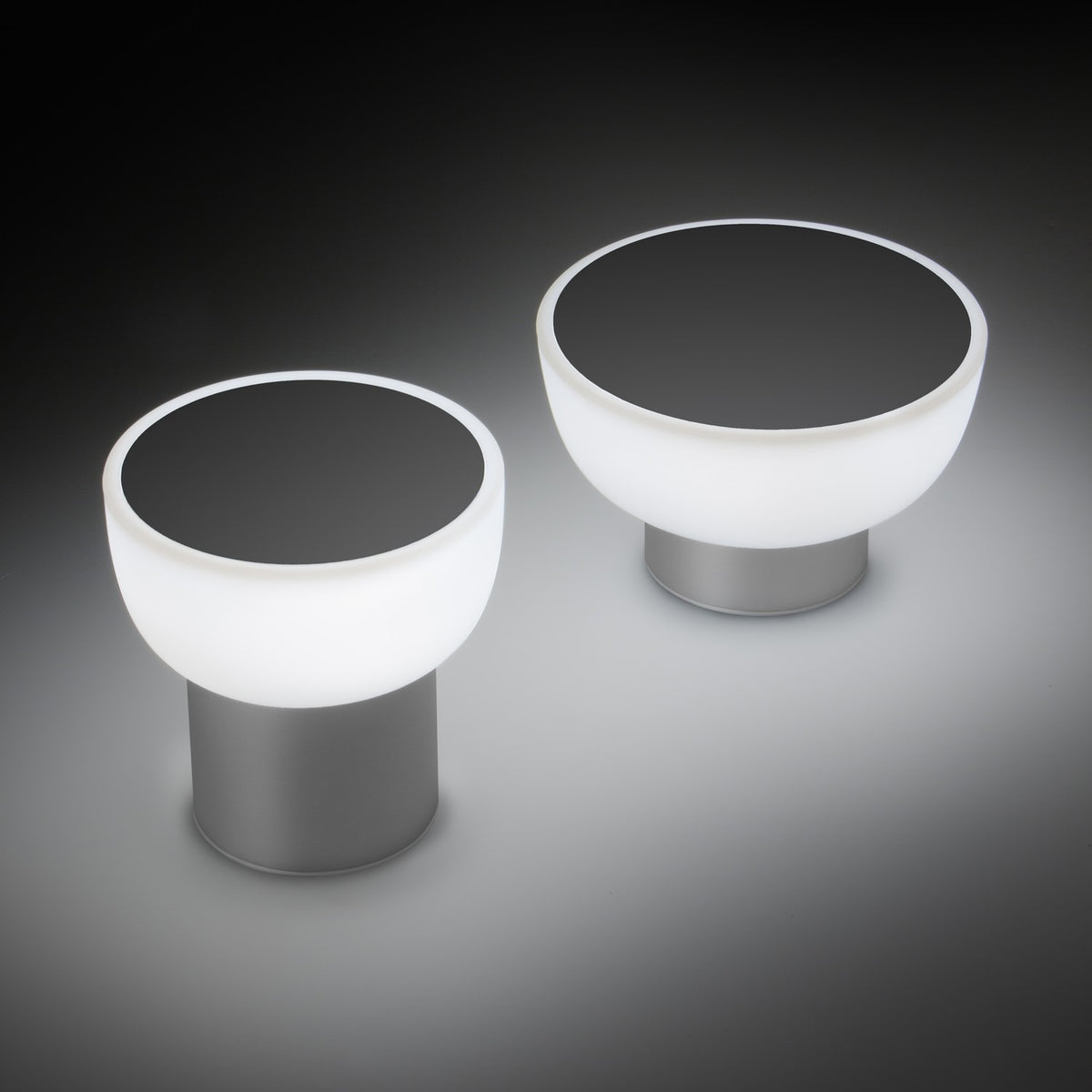 Patio LED rechargeable outdoor table lamp in silver, two sizes shown with rounded opal glass shades, dark top discs, and cylindrical aluminium bases on a dark background.