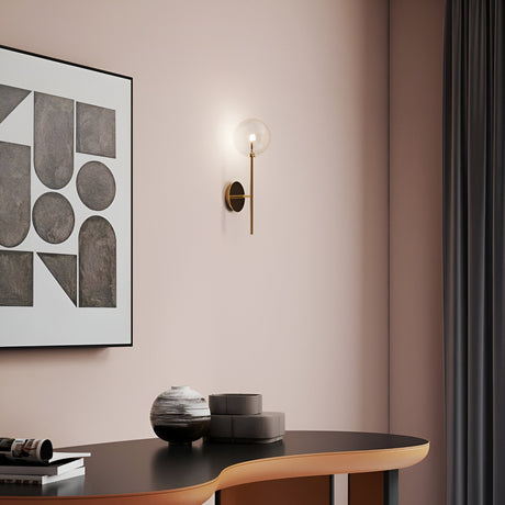 A modern interior features a wall with a geometric art piece and the sleek Solarae Wall Light in a gold finish. A black and wood table below holds decorative objects, including two round containers and a striped vase. A dark curtain hangs on the right.