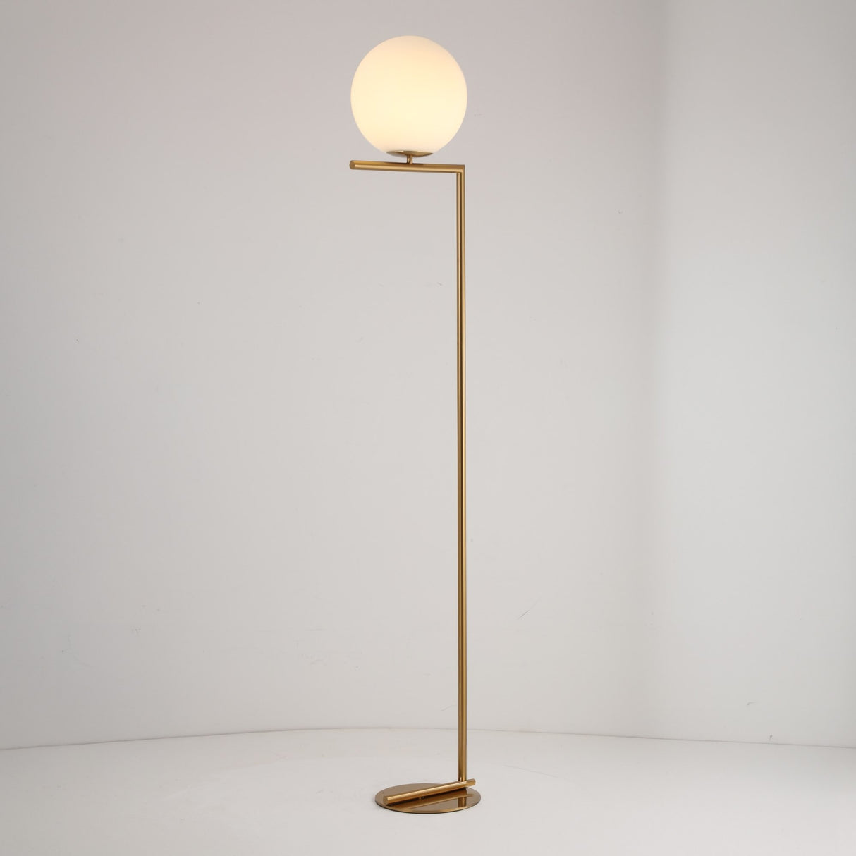 The Vetra 1 Light Opal Glass Floor Lamp features a slim gold stand, an angular base, and a round white opal glass globe lampshade, shown against a plain white background.