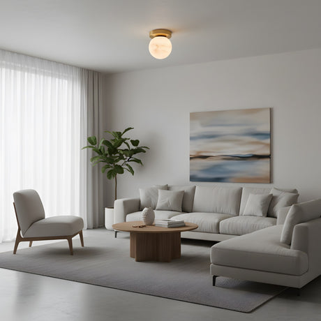 A modern living room featuring a light gray sectional, matching armchair, wood coffee table, potted plant, abstract wall art, and sheer white curtains—centered beneath the Bravora 1 Light Globe Alabaster Semi-Flush in Soft White & Brushed Brass.