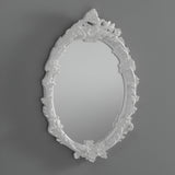 The Mirage Oval Wall Mirror White (64x46cm), featuring a decorative floral and leaf pattern on its white frame, adds vintage style to any plain gray wall.