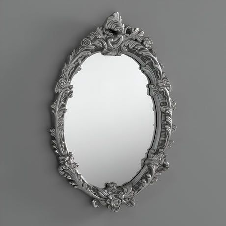 The Mirage Oval Wall Mirror Silver (64x46cm) features a floral-patterned frame, bringing decorative depth and charm to any plain gray wall.