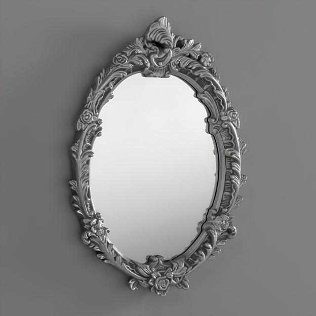 The Mirage Oval Wall Mirror Silver (64x46cm) features a floral-patterned frame, bringing decorative depth and charm to any plain gray wall.