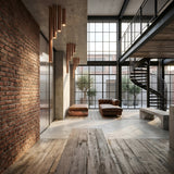 A modern industrial loft with exposed brick walls, large grid windows, wooden floors, a brown leather sofa, minimalist benches, a Pulcra Tube Flush Ceiling Light in copper, and a black spiral staircase leading to a mezzanine.
