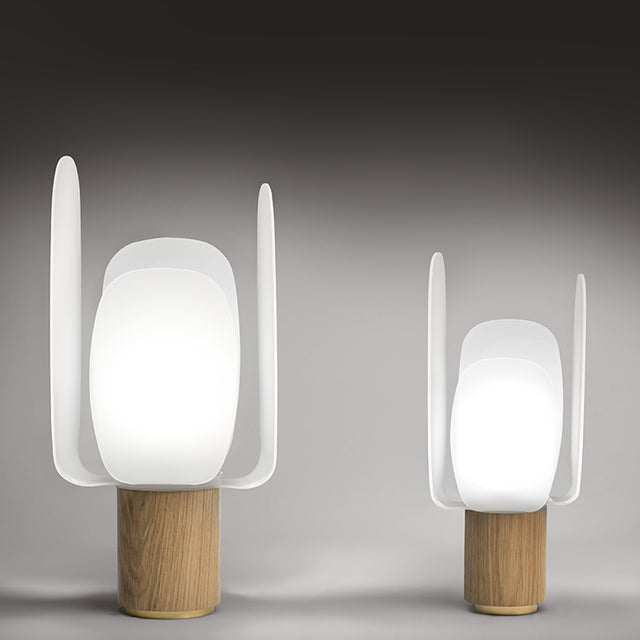 Iselmorne Wooden Table Lamp in two sizes, with white acrylic petal-shaped shade panels around a glowing oval diffuser on a cylindrical oak base, shown against a grey background.