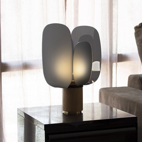 Iselmorne Wooden Table Lamp in Black, with four curved smoked acrylic panels glowing softly atop a cylindrical oak base, shown lit on a side table in a living room setting.