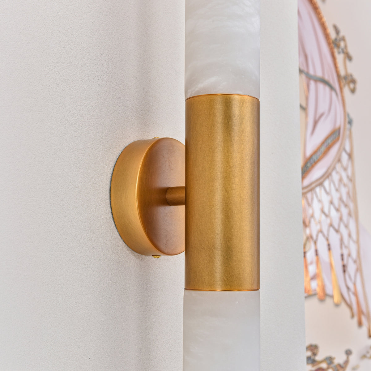 Averin LED Alabaster Wall Light in brushed brass, close-up of the round wall mount and cylindrical bracket joining two alabaster columns.