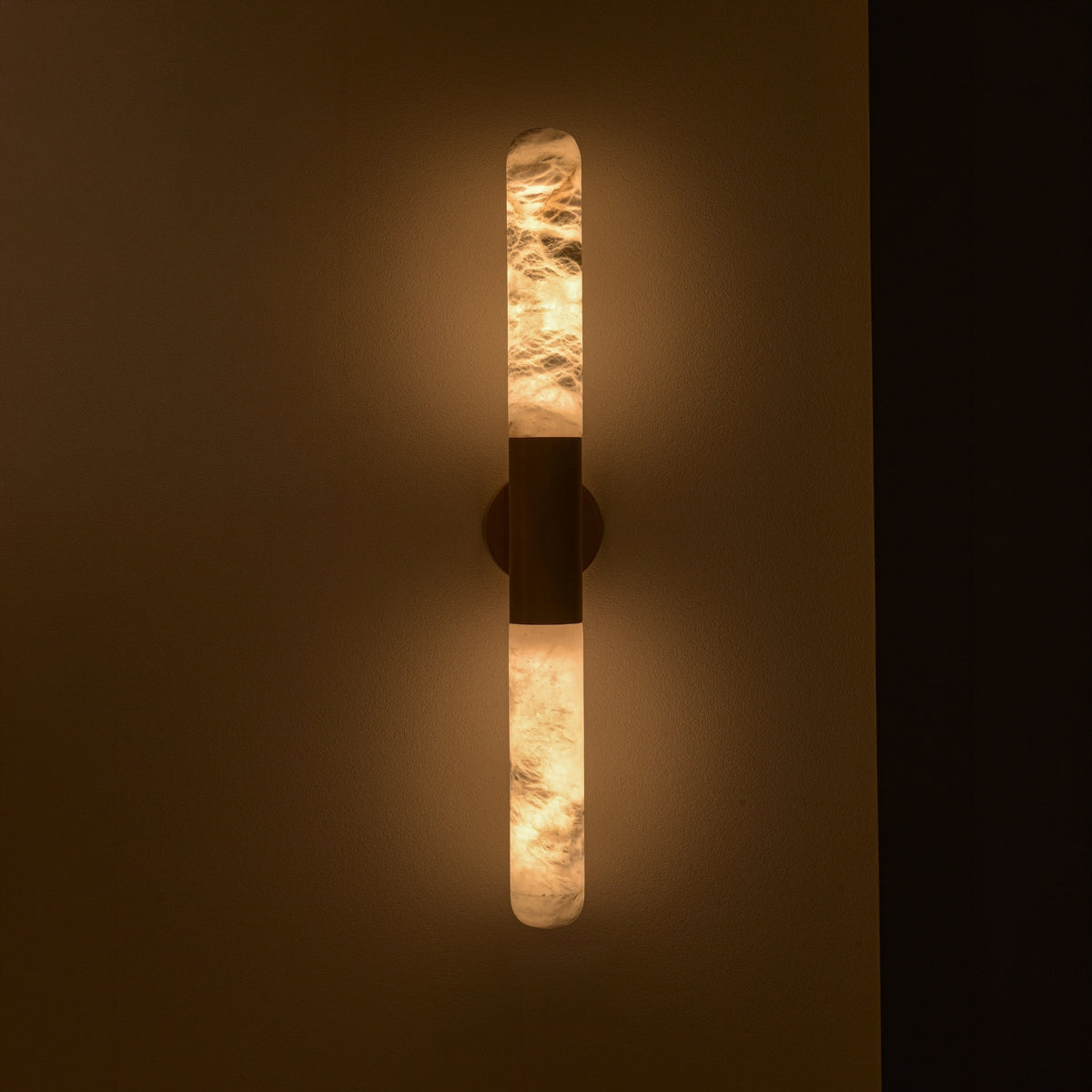 Averin LED Alabaster Wall Light in Brushed Brass, two illuminated vertical alabaster columns joined by a central brass bracket, mounted on a dark wall.
