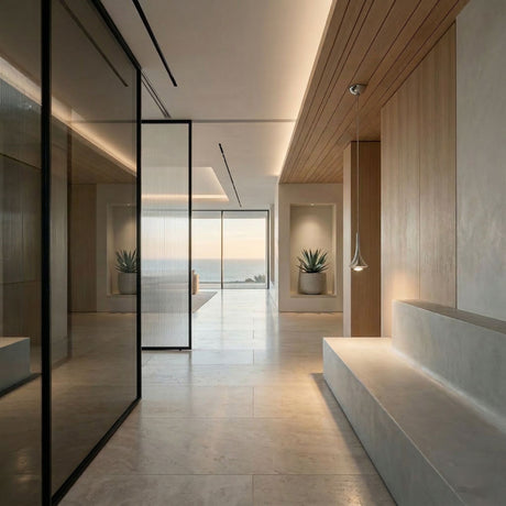 A modern minimalist hallway with stone floors, wood accents, a built-in bench, glass walls, potted plants, and ocean-view windows is elegantly illuminated by the Droplet LED Pendant Light in Chrome.