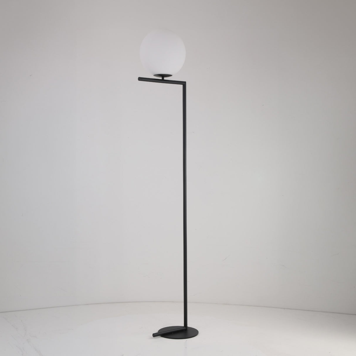 The Vetra 1 Light Opal Glass Floor Lamp in matte black features a minimalist frame and opal glass shade, complementing plain white walls and floors—ideal for contemporary interiors.