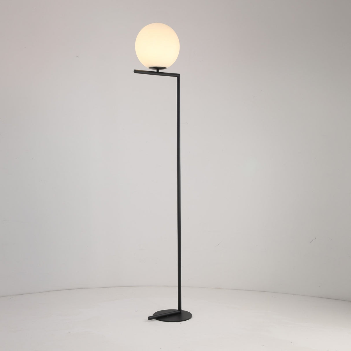 The Vetra 1 Light Opal Glass Floor Lamp in black features a matte finish, slender angular stand, and round opal shade on a circular base, delivering contemporary lighting against a plain white background.