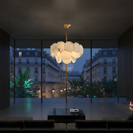 A modern living room with a glass wall overlooking a cityscape at dusk features the Solyra 6 Light 2 Tier Petal Alabaster Chandelier in Soft White hanging above a low coffee table, with large green plants visible outside.