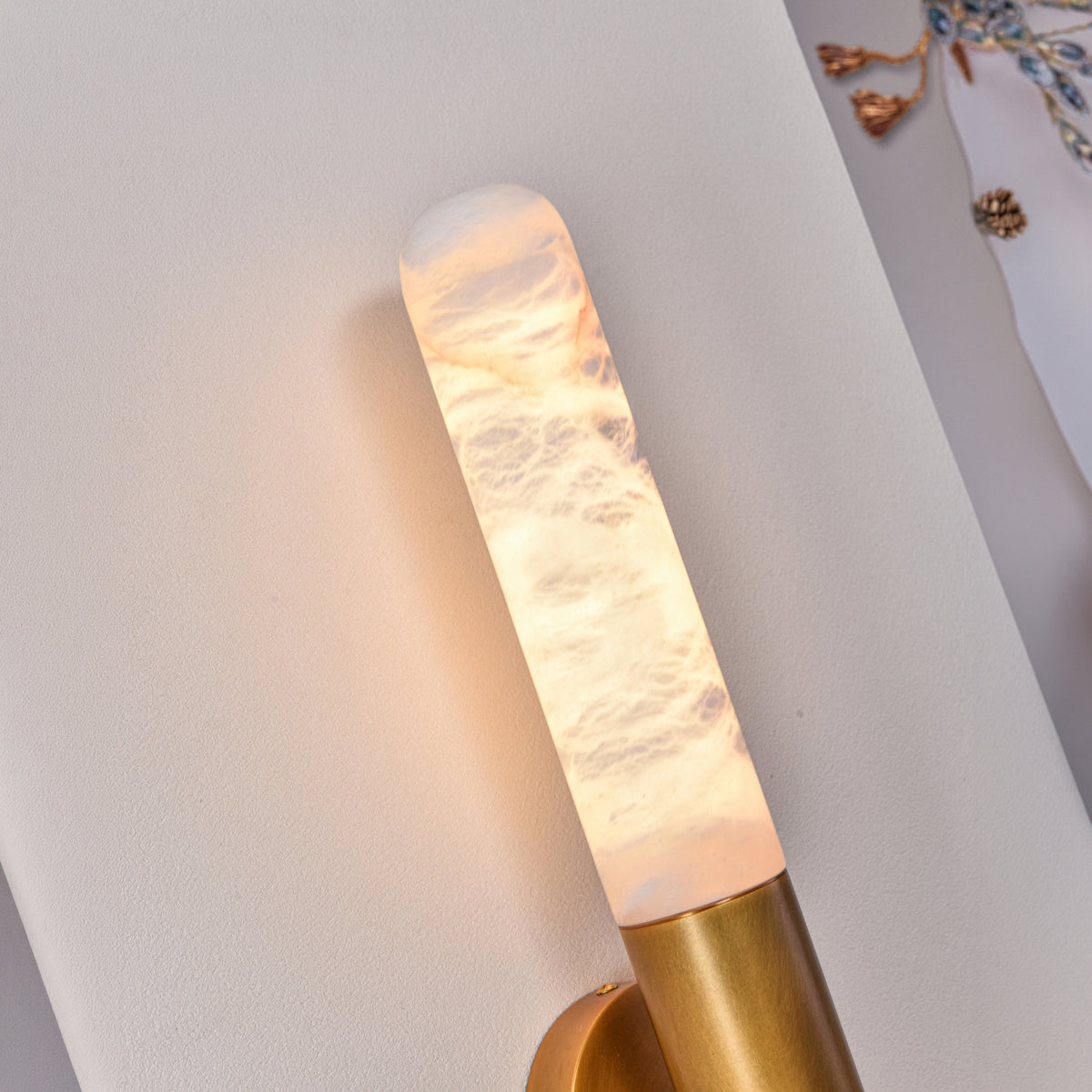 Close-up of the Averin LED Alabaster Wall Light in brushed brass, showing the illuminated natural stone column with warm glow and brass bracket fixing.