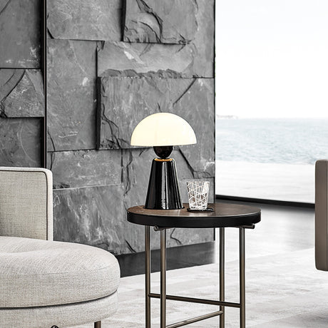 Star Table Lamp in glossy black with white acrylic dome shade on a round side table, shown in a living room with sea-view window and stone wall.