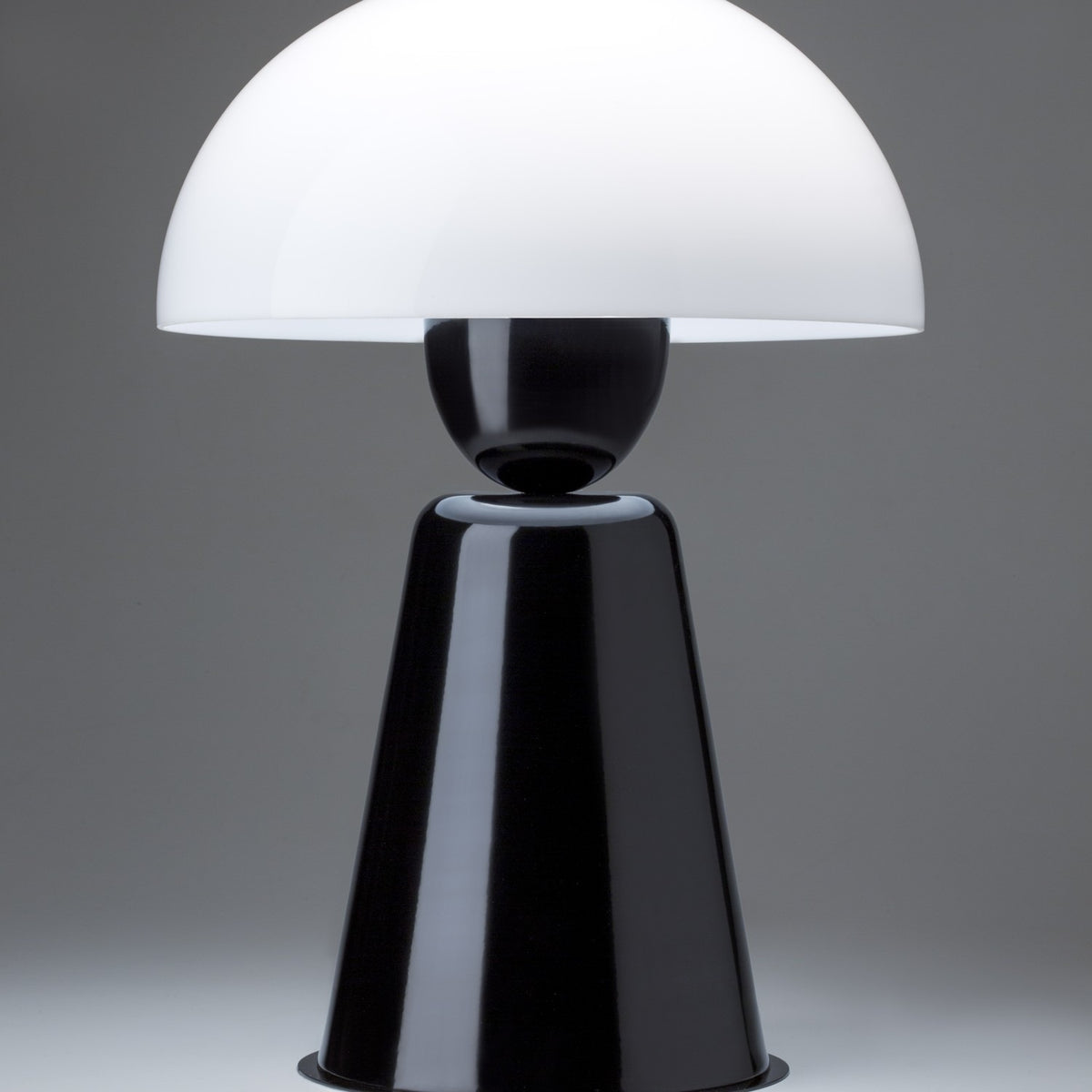 Star Table Lamp in glossy black, close-up of the white acrylic dome shade atop a black sphere joint and tapering iron base, on a plain grey background.