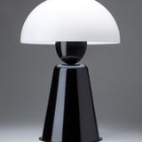 Star Table Lamp in glossy black, close-up of the white acrylic dome shade atop a black sphere joint and tapering iron base, on a plain grey background.