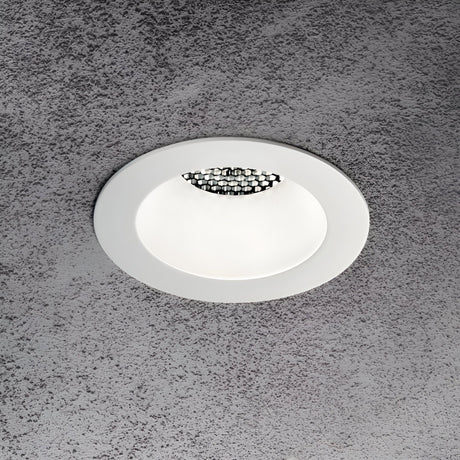 A circular Lumos Downlight Round Frame - White, with a modern design, is installed on a textured grey ceiling. This recessed ceiling light offers ambient lighting and includes decorative elements inside its white rim.