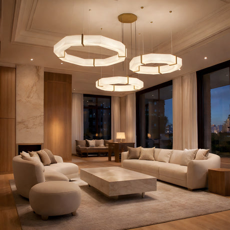 A modern living room with cream sofas, a marble coffee table, city-view windows, and the Vireon LED Triple Ring Alabaster Suspension Light in Bronze & Soft White suspended from a high ceiling. Neutral tones and warm lighting create an inviting atmosphere.