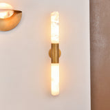 Averin LED Alabaster Wall Light in Brushed Brass, two vertical alabaster columns joined by a brass bracket, glowing warm white on a light wall beside another brass fixture.