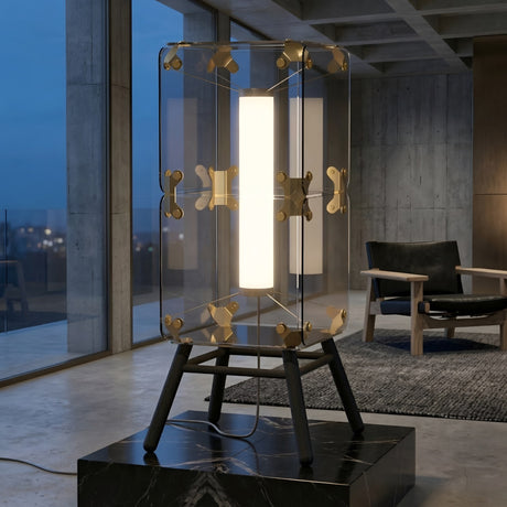 The Qbic LED Large Floor Light - Clear features gold accents and black legs, making it a modern minimalist piece perfect for stylish concrete living rooms with large windows at dusk.