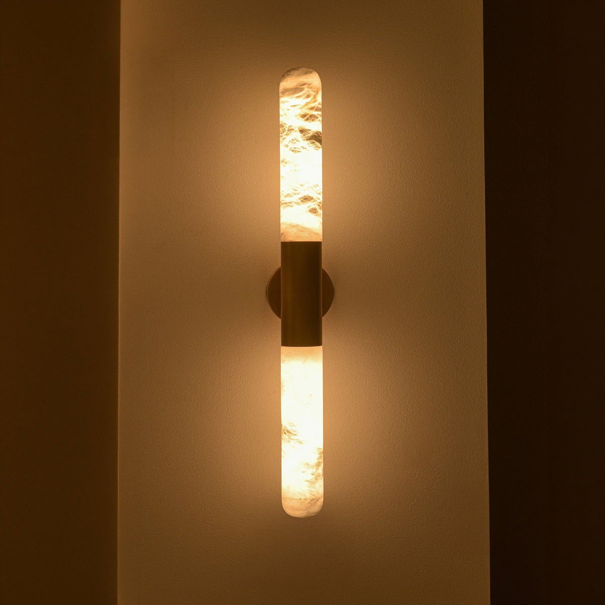 Averin LED Alabaster Wall Light in Brushed Brass, two vertical alabaster columns glowing warm white, joined by a brass centre bracket on a plain wall.