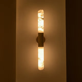 Averin LED Alabaster Wall Light in Brushed Brass, two vertical alabaster columns glowing warm white, joined by a brass centre bracket on a plain wall.
