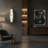 A modern living room with dark walls, abstract art, gray armchair, brass side table, and wooden cabinet features decorative objects illuminated by the Aurelia LED Alabaster Wall Light – Soft White for a soft ambiance.