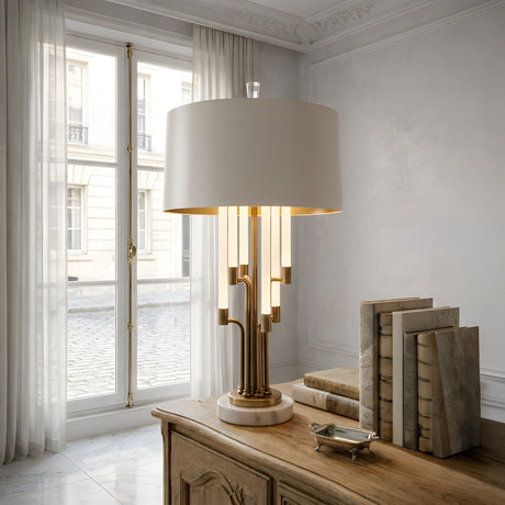 The Calystron 1 Light Branched Alabaster Table Lamp in Brass & Soft White sits on a wooden desk beside books and a tray near a window with sheer curtains, adding elegance and brightness to the room.
