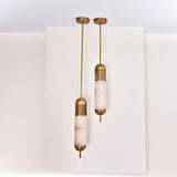 Two Zerith LED alabaster tube pendant lights with fluted brushed brass collars and domed end caps, hung at staggered heights against a white backdrop.