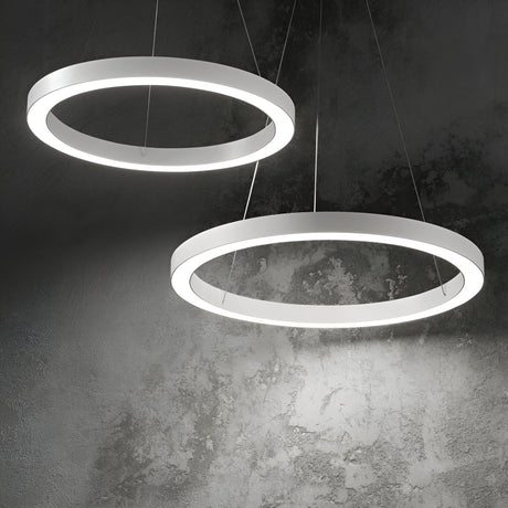 The Arcena Round LED Suspension Lights, with their modern aesthetic, drape elegantly against a textured concrete wall. Crafted with sleek white 70cm frames and energy-efficient dimmable LEDs at 3000K, these fixtures cast a gentle glow that softly highlights the surface behind them, showcasing contemporary lighting design at its finest.