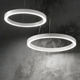 The Arcena Round LED Suspension Lights in a 3000K 50cm white finish hang from the ceiling, illuminating a textured gray wall with their soft glow. Dimmable and circular, these LED fixtures are arranged diagonally, enhancing the space with a sleek and contemporary ambiance.