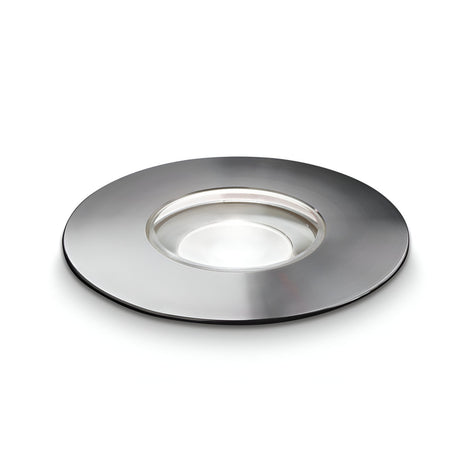 A sleek, round, stainless steel platter with a shallow, glass-like center resembles the Gleamora LED Outdoor Drive Over Recessed Ground Light. Set against a white background, the minimalist design features a reflective metal surface and a transparent central area reminiscent of the Gleamora's modern aesthetic.