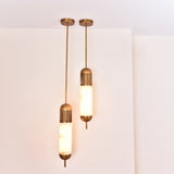 Two Zerith LED alabaster tube pendant lights with brushed brass ceiling mounts and fluted collars, hung at staggered heights against a white wall.