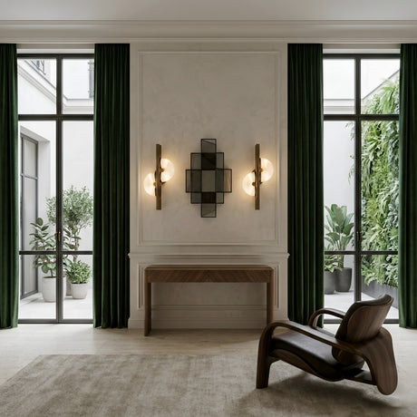 A modern room with tall windows, dark green curtains, indoor plants, a wooden console table, the Lyra LED Twin Disc Alabaster Wall Light in soft white and brushed brass, geometric wall lights, and a sculptural wooden chair on a beige rug.