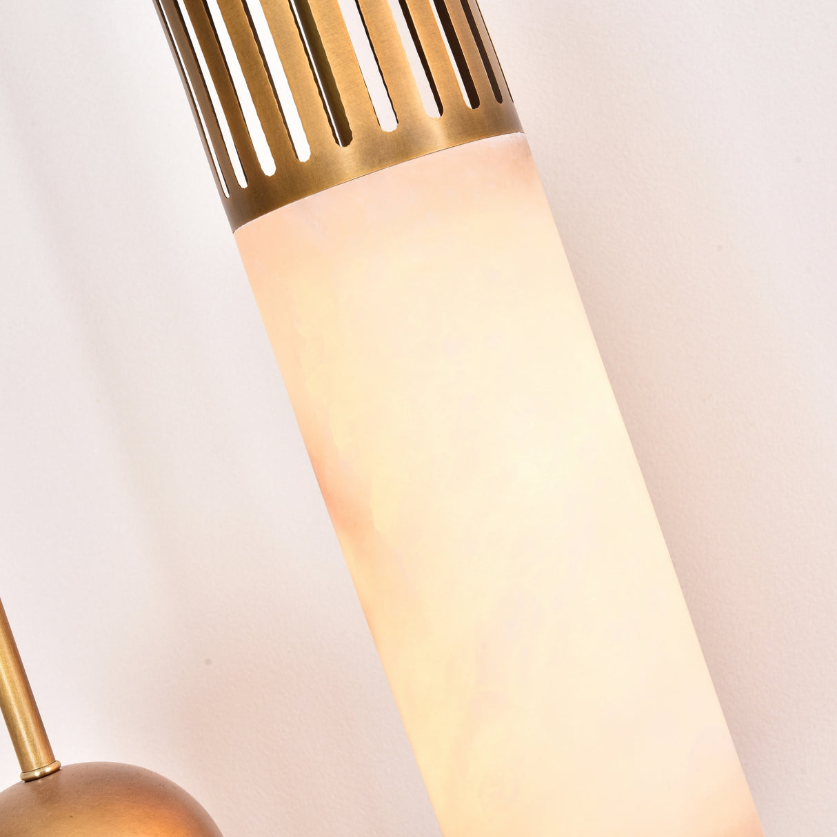 Close-up of the Zerith LED alabaster tube pendant light, showing the natural stone cylinder glowing warm white beneath a fluted brushed brass collar, against a plain light background.
