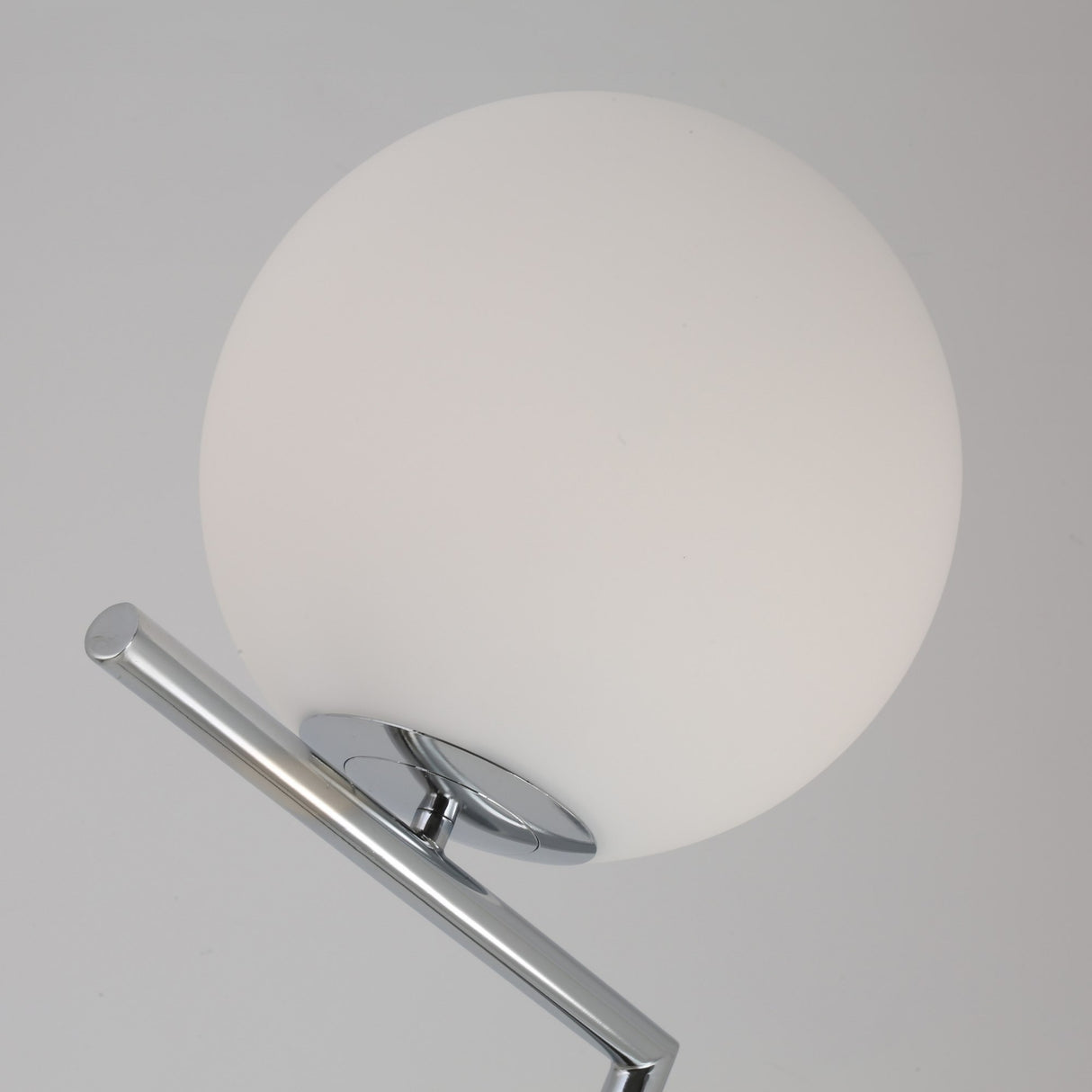 Close-up of the Vetra 1 Light Opal Glass Floor Lamp in grey, featuring an opal glass sphere shade and shiny chrome support, casting soft ambient light against a plain light gray background.